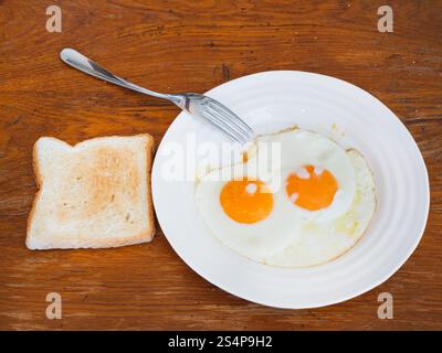 Frühstück mit zwei Spiegeleiern auf weißen Teller und toast auf Holztisch Stockfoto
