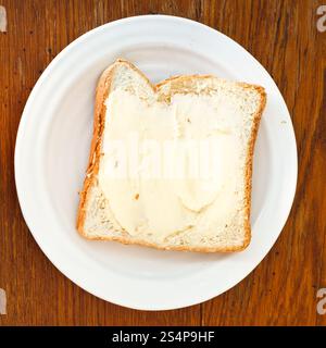 Blick von oben auf Brot und Butter Sandwich auf weißem Teller auf Holztisch Stockfoto