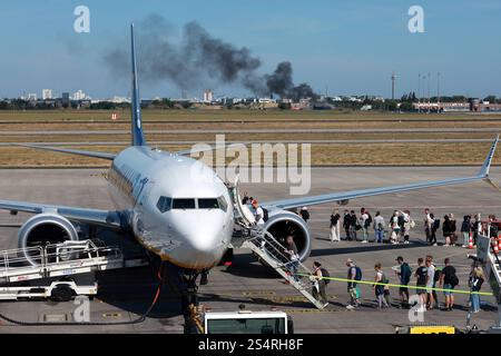 02.09.2024, Schönefeld, Brandenburg, DE - Reisende steigen am Flughafen BER in eine Maschine der Fluggesellschaft Ryanair ein. Im Hintergrund eine Branduebung der Flughafenfeuerwehr. Absturz, Airline, Airport, Alltag, aussen, Aussenaufnahme, Billigflieger, Billigfluggesellschaft, boarden, Boeing, Brand, Brandenburg, Branduebung, Brandwolke, deutsch, Deutschland, einsteigen, Einstieg, Europa, europaeisch, Ferien, Fernreise, Fliegen, Flieger, Flug, Fluggaeste, Fluggesellschaft, Flughafen, Flughafenfeuerwehr, Fluglinie, Flugpassagiere, Flugreise, Flugtechnik, Flugverkehr, Flugzeug, Fl Stockfoto