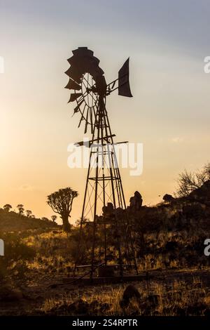 Silhouette einer Windmühle inmitten der felsigen Landschaft mit Köcherbäumen in der trockenen Landschaft am Keetmanshoop in Namibia. Stockfoto