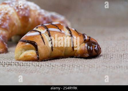 Dieses Makrofoto zeigt drei Croissants auf rustikalem Stoff, mit Puderzucker bestäubt und mit Schokolade getränkt, im Porträt mit Witz präsentiert Stockfoto