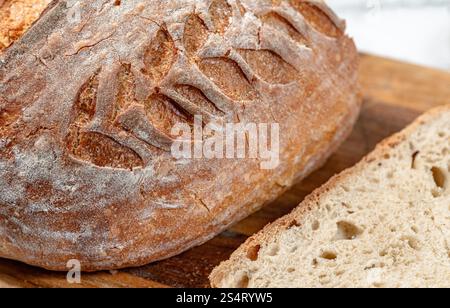Ein detailliertes Bild zeigt einen selbstgemachten Brotlaib, der auf einer Holzoberfläche neben einem Stück liegt. Stockfoto