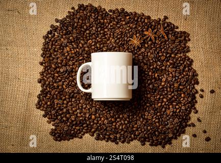 Große weiße Tasse liegen auf Haufen von gerösteten Kaffeebohnen auf Leinentuch Stockfoto