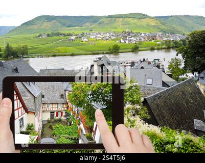 Reisekonzept - Tourist fotografiert traditionelle Häuser in der engen Straße im Dorf Beilstein, Moselregion, Deutschland mit Smartphone, Stockfoto