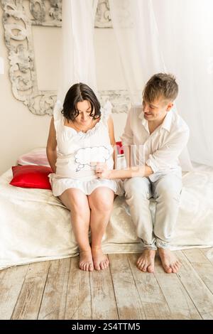Glücklich schwanger paar am Bett sitzen und halten textfreiraum unterzeichnen am Bauch Stockfoto