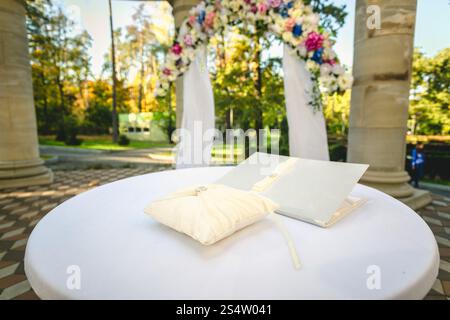 Foto von Eheringen im Freien, die auf Kissen an einem dekorierten Tisch liegen Stockfoto