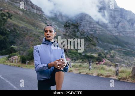 Junge Sportlerin, die sich vor dem Training im Naturpark aufwärmen kann. Selbstbewusste Sportlerin, die ihr Bein im Freien biegt. Stockfoto