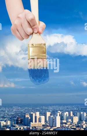 Natur-Konzept - Hand mit Pinsel Farben Blau Himmel über blaue Stadt Stockfoto