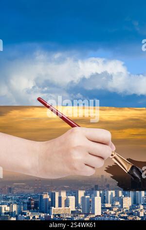 Natur-Konzept - Jahreszeiten und Wetter ändert: Hand mit Pinsel malt Smog Himmel über blaue Stadt Stockfoto