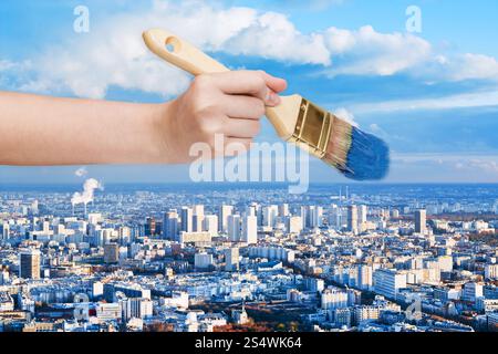 Natur-Konzept - Hand mit Pinsel malt blauen Himmel über Großstadt Stockfoto