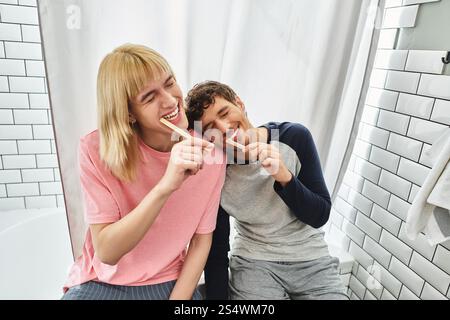 Zwei Männer putzen sich fröhlich die Zähne und lachen in einer einladenden Badezimmerumgebung. Stockfoto