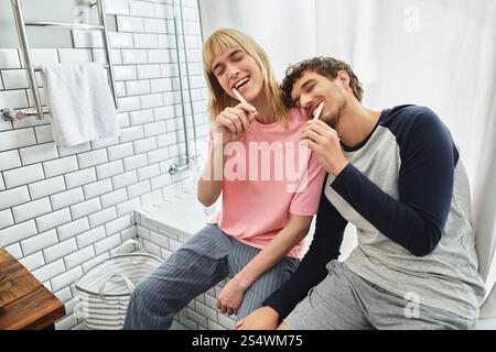 Zwei glückliche Männer putzen sich die Zähne zusammen und teilen sich Lachen und Liebe in einem hellen Badezimmer. Stockfoto