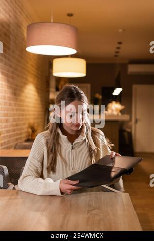 Junge blonde Frau, die im gemütlichen Café einen Laptop aus einer Ledertasche herauszieht Stockfoto