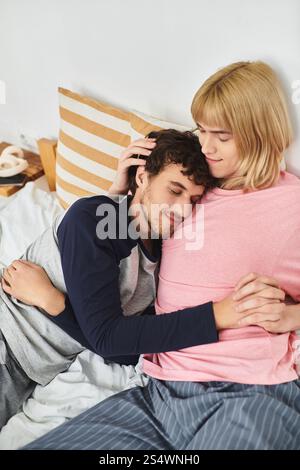 Zwei Männer teilen sich einen zärtlichen Moment, während sie im Bett liegen, in Arme und Lächeln gewickelt. Stockfoto
