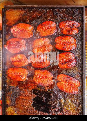 Nahaufnahme von brausenden Chorizo-Würstchen, die auf einer heißen, gewürzten Metallplatte grillen. Stockfoto