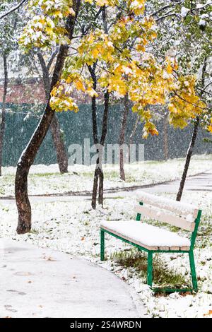 leere Bank im Stadtpark unter ersten Schneefall im Herbst Stockfoto