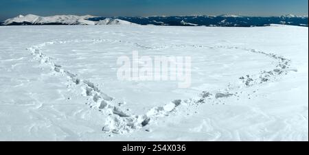 Menschlichen Fußabdruck bilden die Herzform auf schneebedeckten Berg-Plateau und Bergketten hinter. Stockfoto