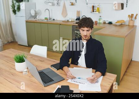 Ein hübscher junger Mann in einem Hemd bewertet Dokumente an seinem stilvollen Arbeitsplatz zu Hause. Stockfoto