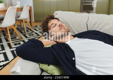 Ein hübscher junger Mann mit lockigen Haaren genießt einen Moment der Entspannung zu Hause. Stockfoto