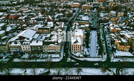 Aus der Vogelperspektive auf ein schneebedecktes Wohngebiet mit Straßen, Häusern und einer Eisenbahnlinie. Das Bild zeigt eine dichte Stadtlandschaft mit einer Mischung Stockfoto