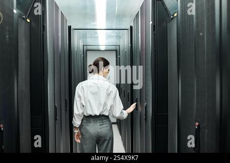 Eine professionelle Frau in einem weißen Hemd arbeitet fleißig zwischen den Server-Racks in einem Rechenzentrum. Stockfoto