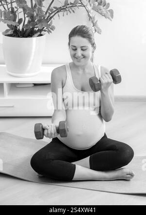 Schwarz / weiß Foto schwangere Frau das Training mit Hanteln zu Hause Stockfoto