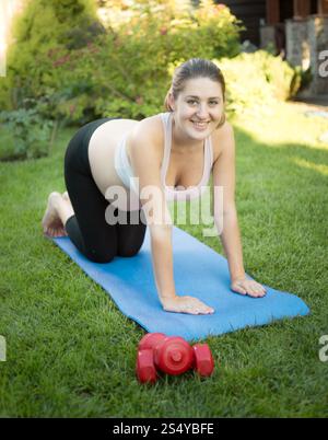 Lächelnde schwangere Frau, die im Park Fitness auf Matte macht Stockfoto