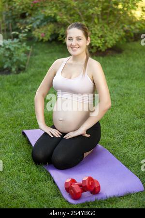 Schwangere Frau, die sich am sonnigen Tag im Park auf dem Gras ausdehnt Stockfoto