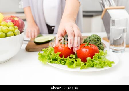 Nahaufnahme Foto einer Frau, die frische Tomaten vom Tisch in der Küche pflückt Stockfoto