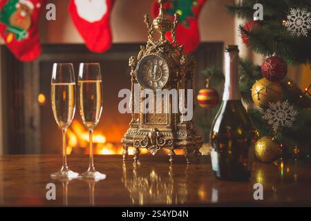 Nahaufnahme von zwei Gläsern Champagner auf dem Tisch neben der alten Uhr, die Mitternacht im weihnachtlich dekorierten Wohnzimmer zeigen Stockfoto