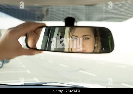 Nahaufnahme einer Frau, die den Autospiegel verstellt und in die Reflexion schaut Stockfoto