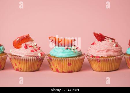 Nahaufnahme von bunten Cupcakes mit Streuseln und frischer Erdbeere in Reihe Stockfoto