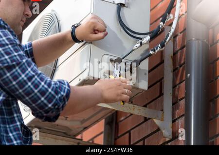 Männlicher Techniker, der die Klimaanlage im Freien repariert Stockfoto
