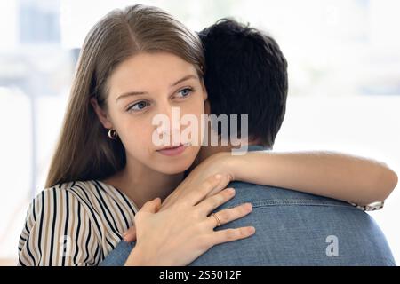 Nachdenklich gestresste, schöne junge Frau, die den Ehemann umarmt Stockfoto