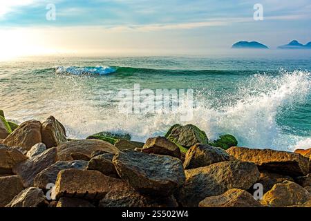 Die Wellen brechen bei Sonnenaufgang in Rio de Janeiro gegen die Felsen des Grenzbruchs Barra da Tijuca Stockfoto