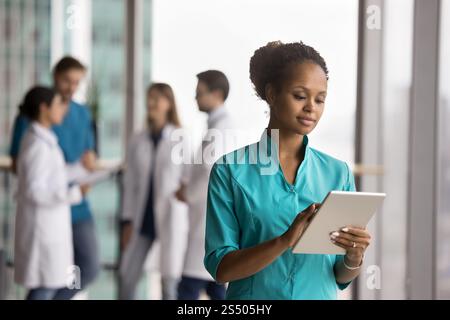 Fokussierter afrikanischer Arzt in Peelings-Uniform mit Tablette gekleidet Stockfoto