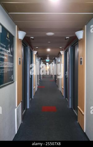 Warschau, Polen - 13. Juni 2024: Langer und dunkler Korridor in einem kleinen Hotel mit grauen Türen auf beiden Seiten, kleinen Lampen und wenigen Plakaten an den Wänden Stockfoto