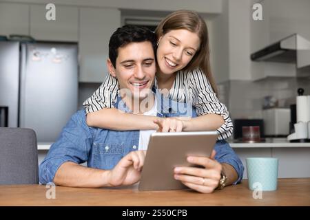Glückliches junges Paar mit digitalem Tablet am Küchentisch zu Hause Stockfoto