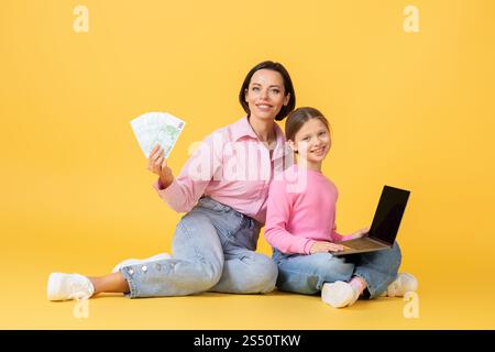 Mutter und Tochter knüpfen zusammen, während sie drinnen an einem Laptop arbeiten Stockfoto