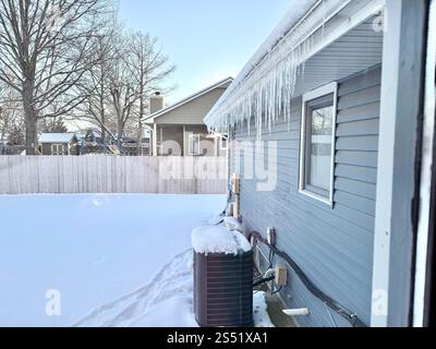 Starker Schnee und Sonnenschein verursachen Schmelzen und Eiszapfenbildung auf Traufe, ein Eisdamm, der zu Dachleckagen führen kann. Wichita, Kansas, USA. Stockfoto