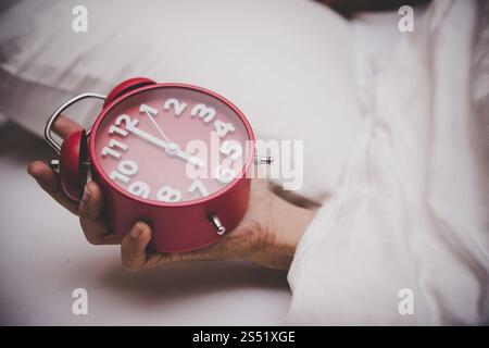 Mann im Bett, der den Wecker auf 6 Uhr stellt. Stockfoto