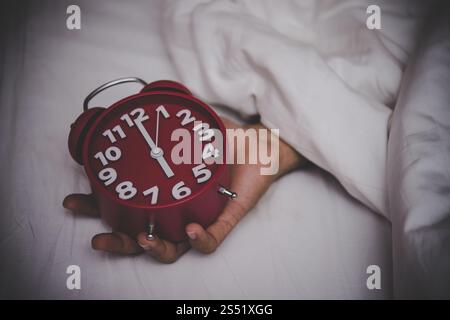 Mann im Bett, der den Wecker auf 6 Uhr stellt. Stockfoto