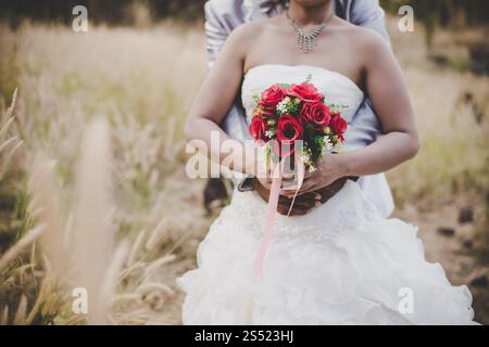 Die Braut hält einen Brautstrauß in die Hände, der Bräutigam umarmt sie von hinten. Hochzeit Liebhaber Konzept. Stockfoto