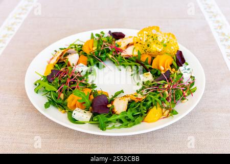 Dieser lebhafte Salat besteht aus einer Mischung aus Gemüse, geschnittenen Früchten und essbaren Blumen, die künstlerisch auf einem weißen Teller angeordnet sind. Ein gesundes Gericht perfekt für jeden Stockfoto