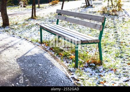 Leeren Bank in der Nähe von Fußweg in städtischen Garten mit dem ersten Schnee im frostigen Herbst Tag abgedeckt Stockfoto