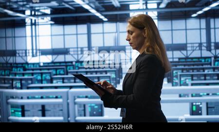 Computerwissenschaftler, der die Überprüfung durchführt und Daten auf Tablets mit den erforderlichen Fehlerbehebungen im Server-Hub eingibt. Frau, die im Rechenzentrum arbeitet und eine fortschrittliche Datenspeicherinfrastruktur zur Unterstützung von IT-Workloads bietet, Kamera A Stockfoto