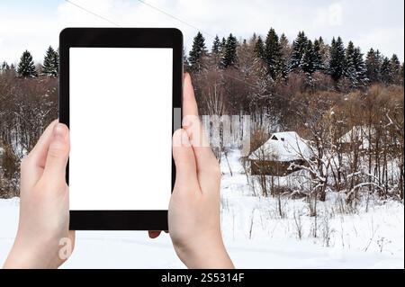 Reisekonzept - touristische Fotos des russischen Dorfes in der Nähe des Waldes am bewölkten Wintertag in der Region Smolensk in Russland auf Smartphone mit Ausschnitt Stockfoto