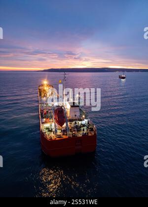 Aus der Vogelperspektive eines hell beleuchteten Tankschiffes auf dem Meer während der Dämmerung, umgeben von offenem Wasser und einem leuchtenden Horizont Stockfoto