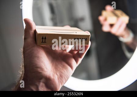 Paris, Frankreich - 22. November 2022: Hand hält ein kleines Amazon-Paket vor einem Spiegel, das das Logo und die Verpackungsdetails reflektiert, in einem leisen Licht Stockfoto