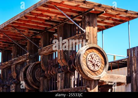 Eine Holzkonstruktion mit einem großen Rad oben. Das Gebäude scheint alt und rustikal zu sein Stockfoto